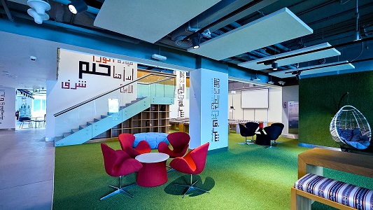 Inside the Khalifa Innovation Center: a bright co-working space with Arabic calligraphy on the walls, green carpet and red lounge chairs.